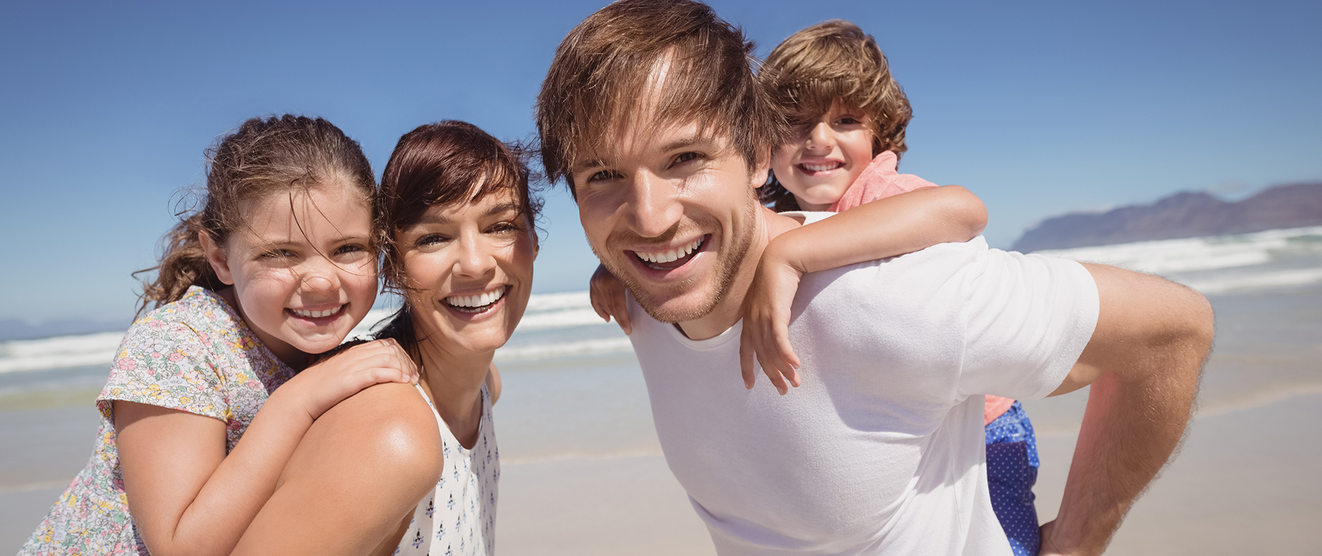 Portrait of family smiling together at beach against clear blue sky