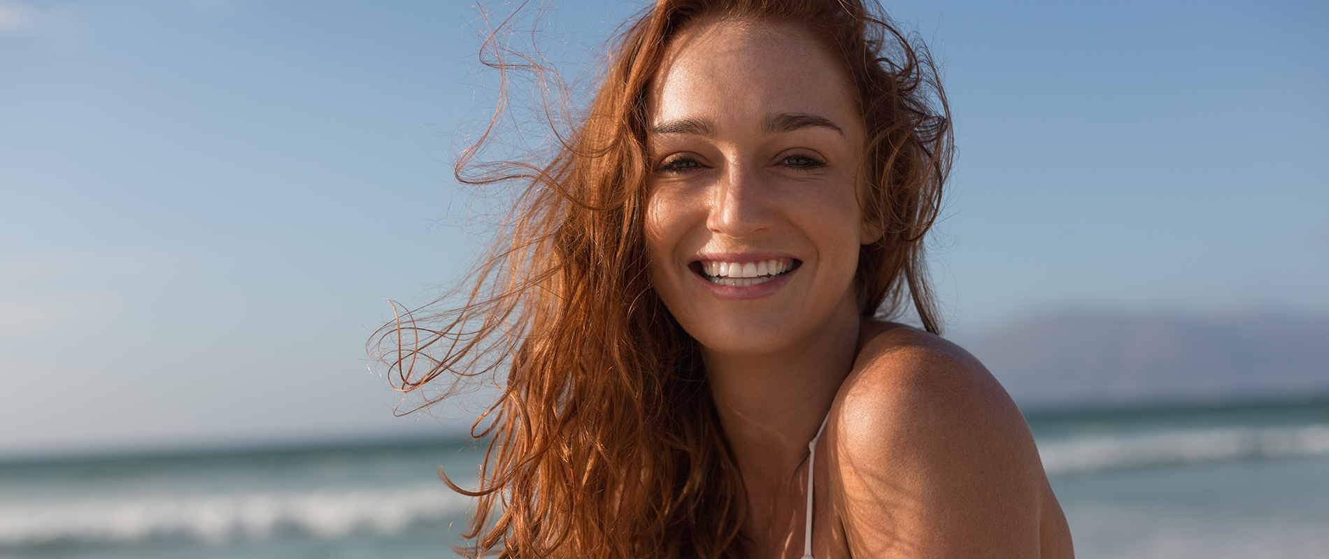 Front view of beautiful happy young Caucasian woman looking at camera standing on the beach. She is smiling